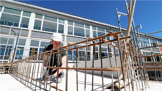 Ein Bauarbeiter arbeitet im Sonnenschein auf einem Rohbau.