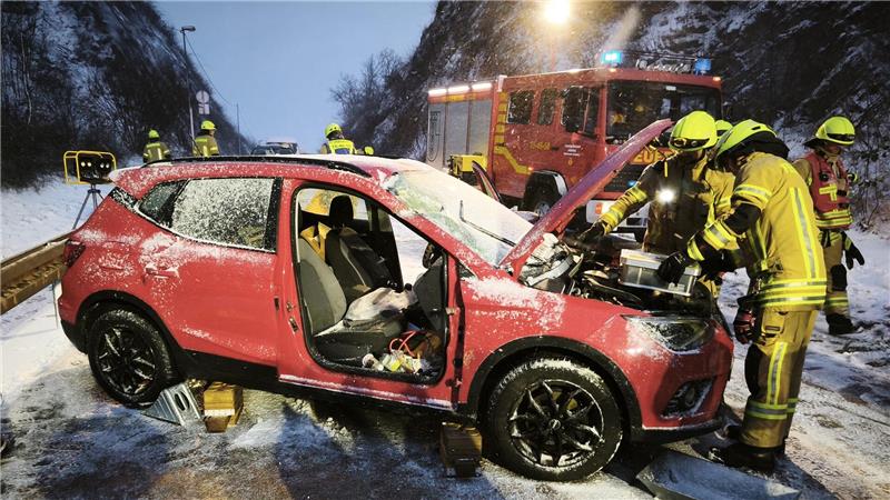 Einsatzkräfte der Feuerwehr beugen sich über den Motorraum eines Unfallwagens.