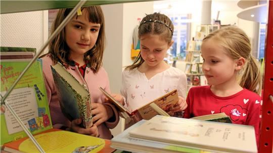 Drei Kinder schauen sich in der Stadtbibliothek die Bücherauswahl an: Nach einem gelesenen Buch sind die Teilnehmer „Leseprinzen“, nach fünf Titeln „Lesekönige“ und nach zehn „Lesekaiser“. 