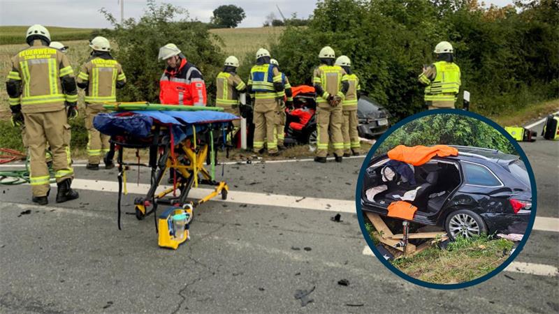 Einsatzkräfte der Feuerwehr stehen auf der Straße, an der sich ein Unfall ereignet hat. Ein Auto liegt im Graben