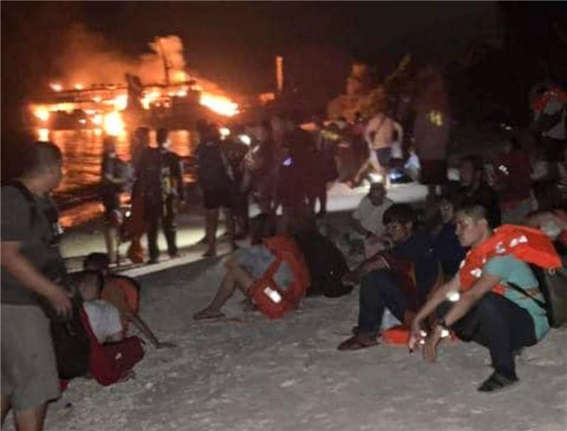 Philippinen: Noch Vermisste nach Inferno auf Passagierfähre Nach ihrer Rettung ruhen sich Überlebende an Land aus. Im Hintergrund ist die brennende Fähre zu sehen.