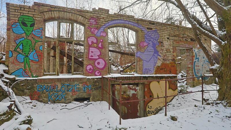 Verfallenes Backsteingebäude mit großen Fensteröffnungen und bunten Graffiti an den Wänden im verschneiten Wald