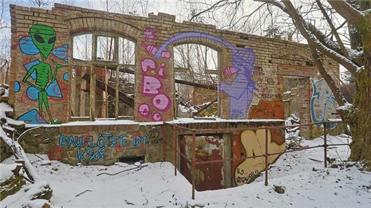 Verfallenes Backsteingebäude mit großen Fensteröffnungen und bunten Graffiti an den Wänden im verschneiten Wald