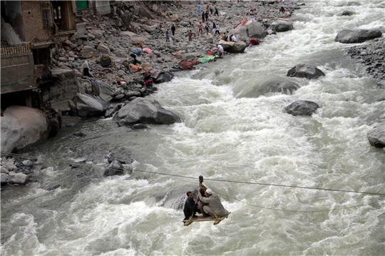 Nach schweren Überschwemmungen überqueren Menschen im pakistanischen Bahrain einen Fluss mithilfe einer Seilbahn.