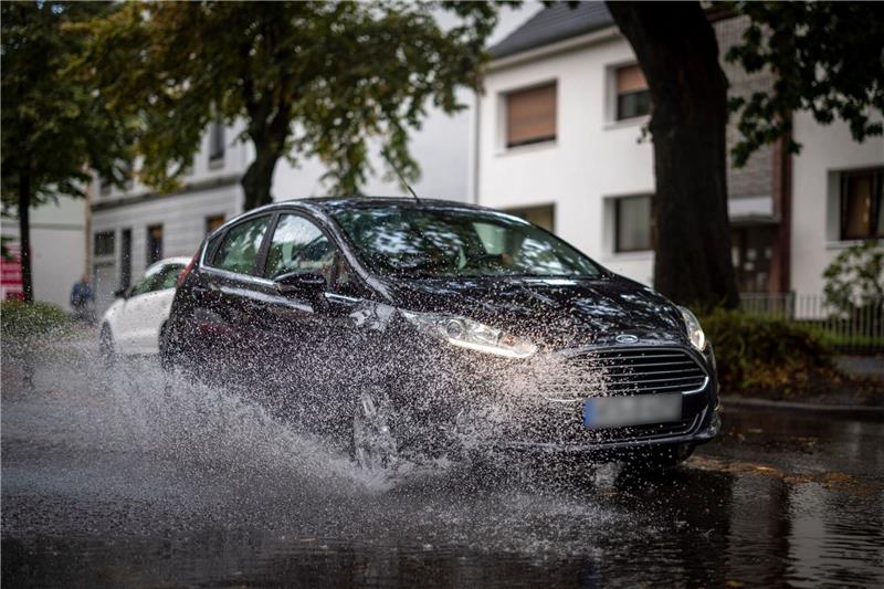 Teils kräftige Gewitter mit Starkregen und Hagel möglich Nach starken Regenfällen am Dienstagmorgen fährt ein Auto durch eine große Pfütze in Duisburg.