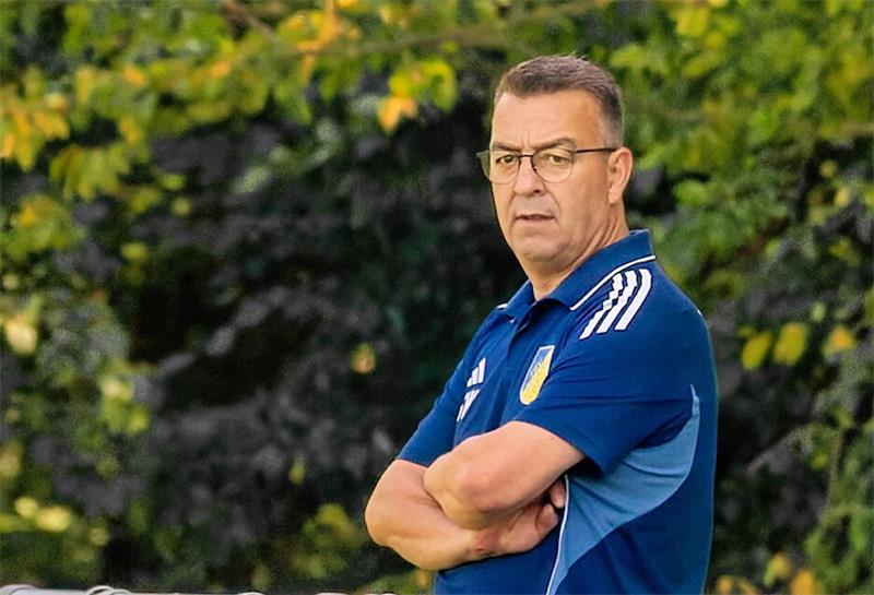 Trainer in blauem Sportoutfit steht mit verschränkten Armen vor einer Werbebande