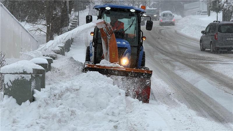 Das Foto zeigt einen schmalen Schneepflug, der auf einem Gehweg fährt.