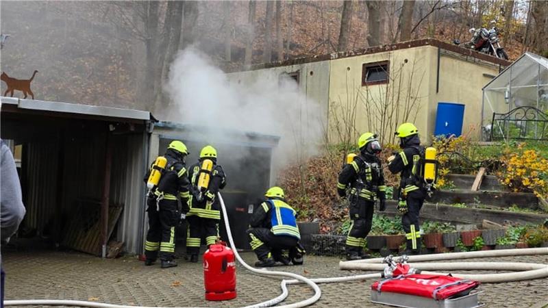 Fürnf Feuerwehrmänner stehen vor einer qualmenden Garage und löschen diese mit einem Wasserschlauch.