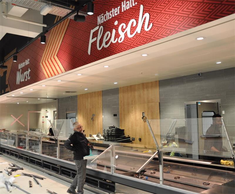 Ein Mann steht vor einer noch leeren Fleischtheke mit großen Schildern.
