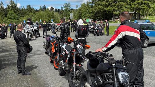 Dsa Foto zeigt mehrere Motorradfahrer, die an ihren Maschinen stehen. Im Hintergrund sind auch Polizeibeamte zu sehen.