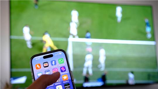 Nebenbei mal daddeln: Während das Fußballspiel läuft, schauen viele Zuschauer nebenbei aufs Handy. (Symbolbild)