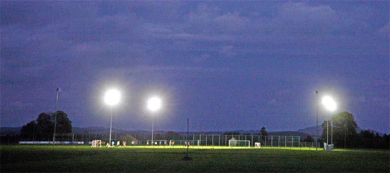 Fußballfeld bei Nacht mit hell erleuchteten Flutlichtmasten unter bewölktem Himmel 