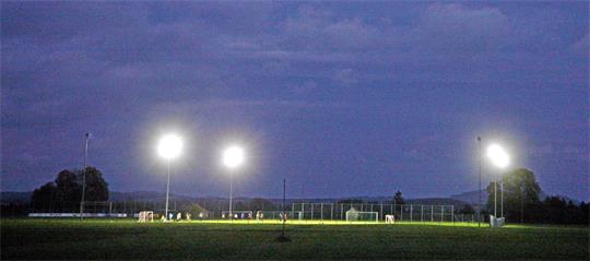Fußballfeld bei Nacht mit hell erleuchteten Flutlichtmasten unter bewölktem Himmel 