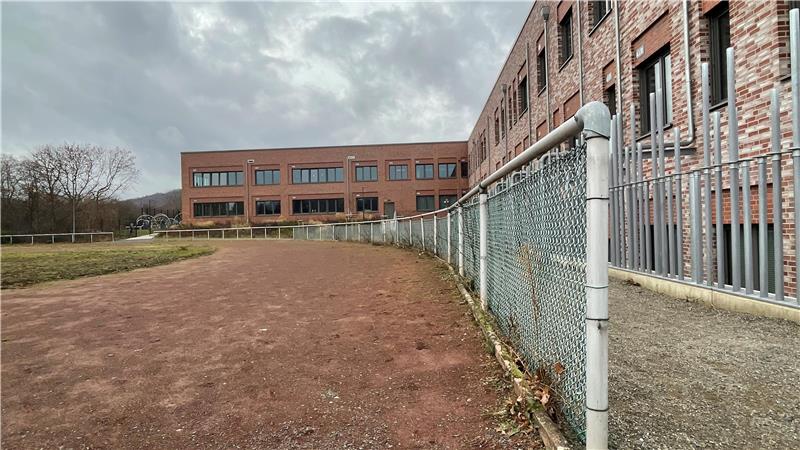 Das Foto zeigt  links den Sportplatz mit rötlicher alter Aschenbahn neben dem modernen neuen Schulzentrum Goldene Aue rechts.