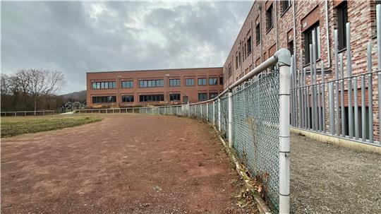 Das Foto zeigt  links den Sportplatz mit rötlicher alter Aschenbahn neben dem modernen neuen Schulzentrum Goldene Aue rechts.
