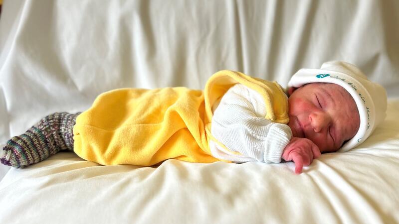 Ein Baby in einem gelben Strampler gekleidet, liegt auf dem Bauch und schläft.