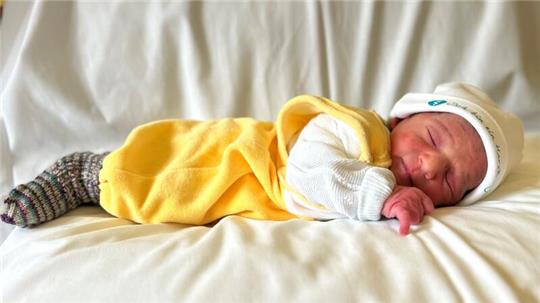 Ein Baby in einem gelben Strampler gekleidet, liegt auf dem Bauch und schläft.