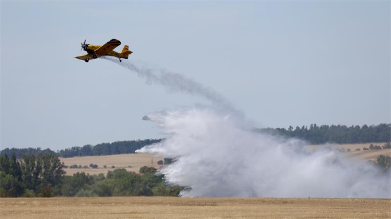 Ein Löschflugzeug fliegt über ein Feld und wirft Wasser ab.