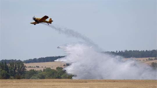 Ein Löschflugzeug fliegt über ein Feld und wirft Wasser ab.