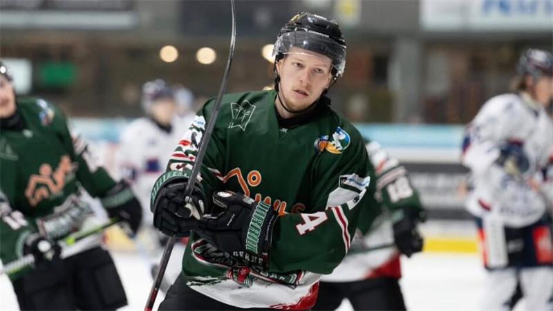 Eishockeyspieler in grünem Trikot und Helm auf dem Eis, im Hintergrund weitere Spieler in unterschiedlichen Trikots