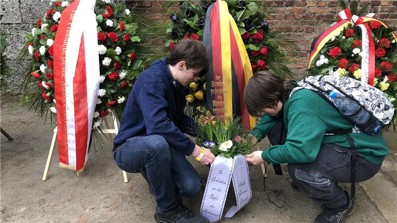Schüler der Okeraner Adolf-Grimme-Schule fahren nach Auschwitz Noah Wolf (l) und Luca Meyer legen das mitgebrachte Blumengesteck vor der Todeswand nieder, während Emily Berger eine kurze Rede hält.
