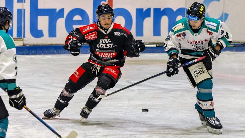 Drei Eishockeyspieler in Aktion auf dem Eis, zwei in weißen Trikots und einer in schwarzem Trikot mit roten Akzenten, alle mit Schlägern und Blick auf die Puck.