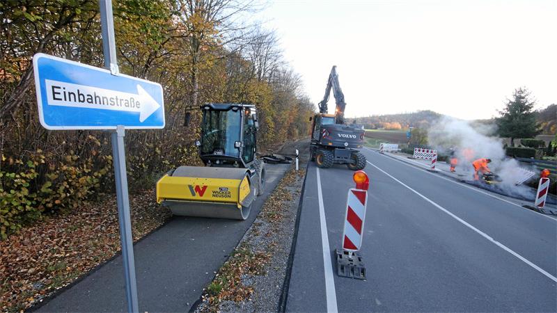 Straßenszene mit Baustelle, Baumaschinen und einem Schild mit der Aufschrift 'Einbahnstraße'