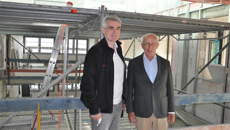 Zwei Männer stehen in einem Rohbau mit Metallgerüst und Leiter im Hintergrund