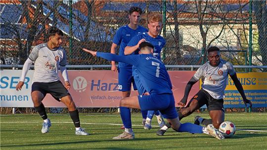 Vier Fußballspieler auf einem Spielfeld kämpfen um den Ball, zwei in blauen Trikots und zwei in weißen Trikots