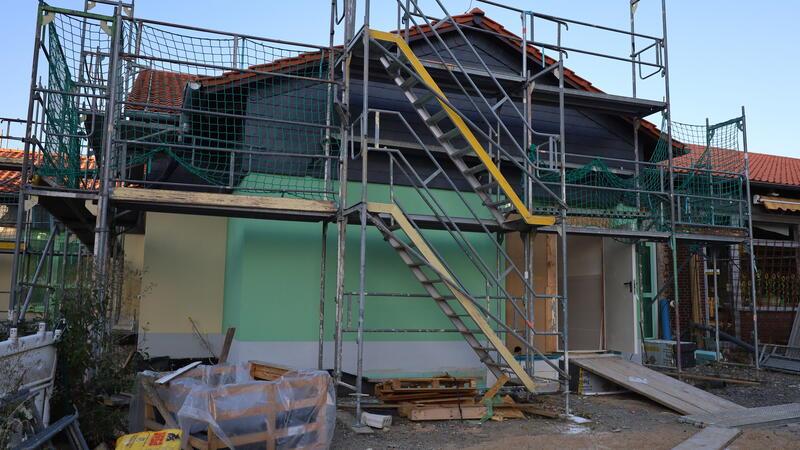 Haus mit Gerüst und Baustoffen davor in einer Baustelle