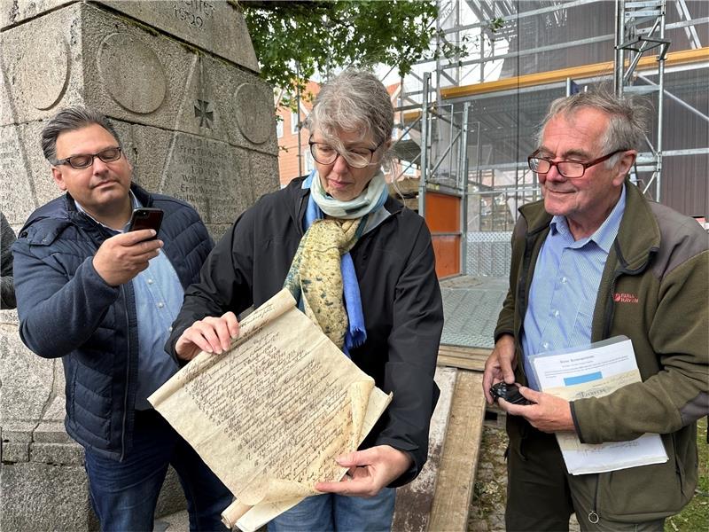 Braunlage: Kirche sichert Schätze aus der Zeitkapsel Noch vor Ort am Fuße des Turms der Trinitatiskirche öffnet Pfarrerin Kirstin Müller im Beisein von Bürgermeister Wolfgang Langer (links) und Dr. Hans-Ulrich Bonewitz die Zinkrolle und präsentiert den interessierten Zuschauern die Namen der Pastoren, die seit 1788 in Braunlage gearbeitet haben. Foto: Eggers