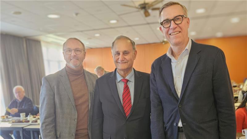 Drei Männer in Anzügen stehen in einem Raum nebeneinander.