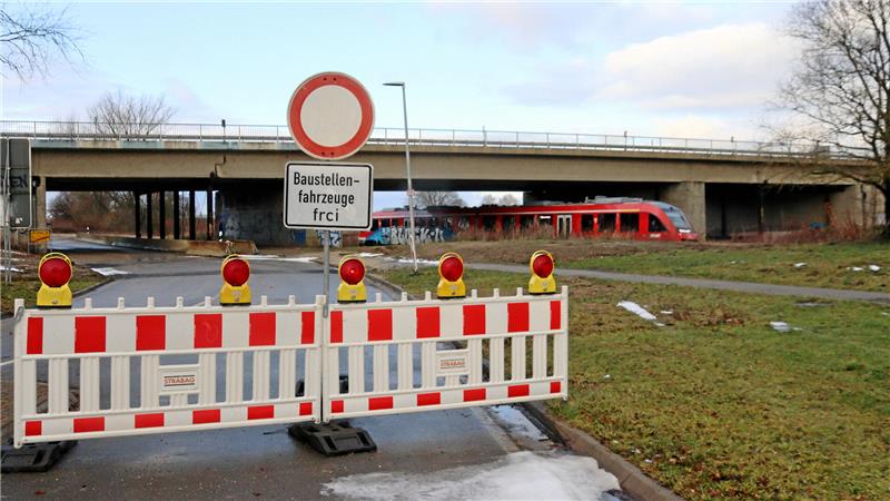 Ein Zug fährt unter einer gesperrten Brücke hindurch.
