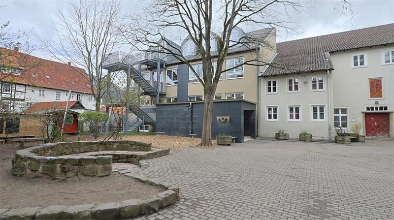 Innenhof mit gepflastertem Boden, Sandkasten mit Steinumrandung und mehreren Gebäuden im Hintergrund
