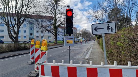 Rote Ampel an einer Straßensperrung mit Absperrungen und einem Verkehrsschild, das auf einen Fußweg mit Kindern nach links weist.