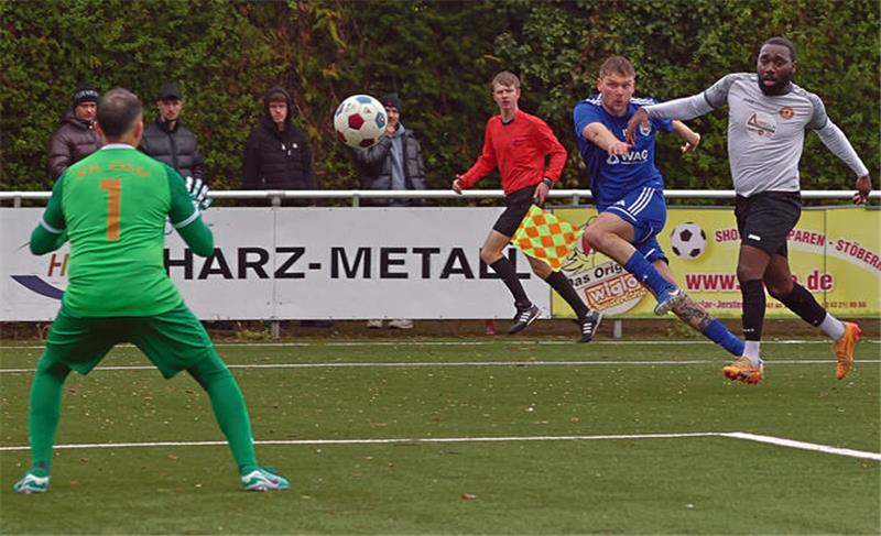 Zwei Fußballspieler im Zweikampf vor dem Tor, ein Spieler in grünem Torwarttrikot beobachtet den Ball.