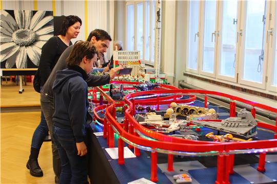 Eine Familie steht an einem großen Legoparcours; der Mann in der Mitte fotografiert Details mit dem Handy.