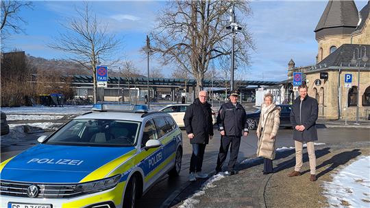 Polizeiauto mit blau-gelber Beklebung steht auf schneebedecktem Gehweg vor einem historischen Gebäude, daneben vier Personen in Winterkleidung