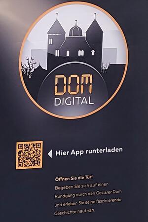 Ein Plakat mit QR-Code weist auf die neue App "Dom:Digital" hin