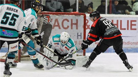 Eishockeyszene vor dem Tor mit Torwart in weiß-türkis und Angreifer in schwarz-rot, mehrere Spieler in Aktion auf dem Eis