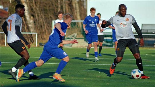 Fußballspieler in blauen und weißen Trikots kämpfen um den Ball auf einem Spielfeld mit Kunstrasen