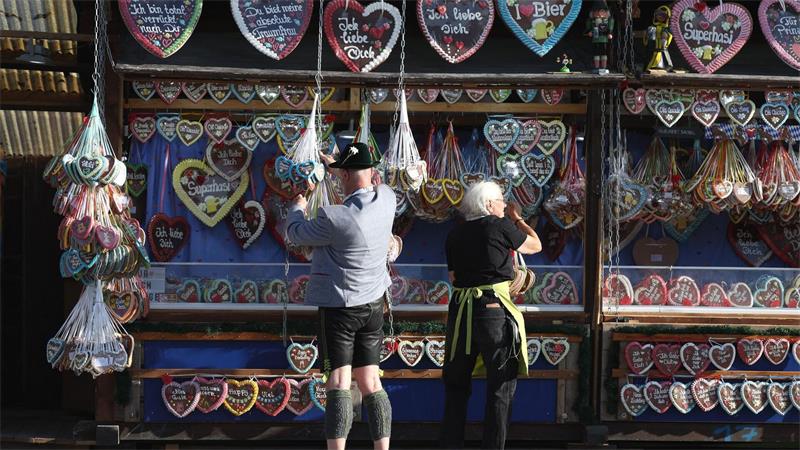Oktoberfest 2026: Mann in Tracht vor Lebkuchenherzen auf der Wiesn
