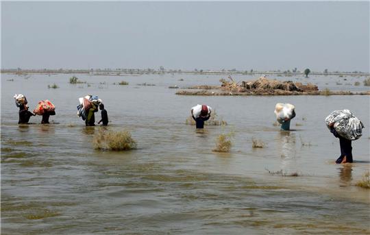 Opfer der schweren Überschwemmungen durch Monsunregen tragen in der Provinz Sindh Hilfsgüter durch das Hochwasser.