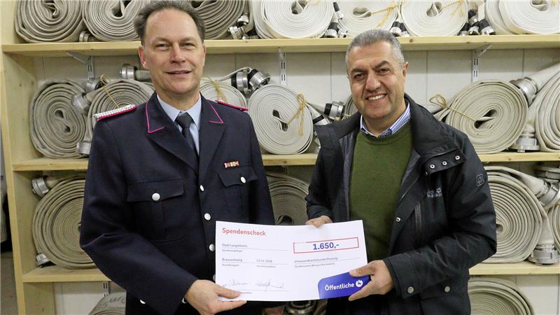 Zwei Personen präsentieren vor Feuerwehrschläuchen einen symbolischen Scheck.