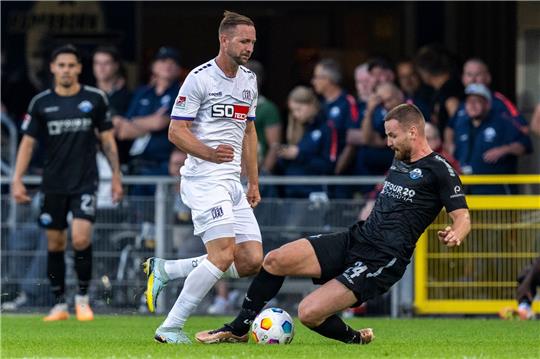 Osnabrücks John Verhoek (M) und Paderborns Jannis Heuer kämpfen um den Ball.