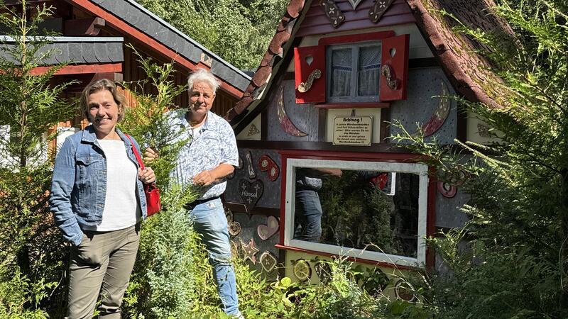 Eine Frau und ein Mann stehen vor einem Märchenhaus.