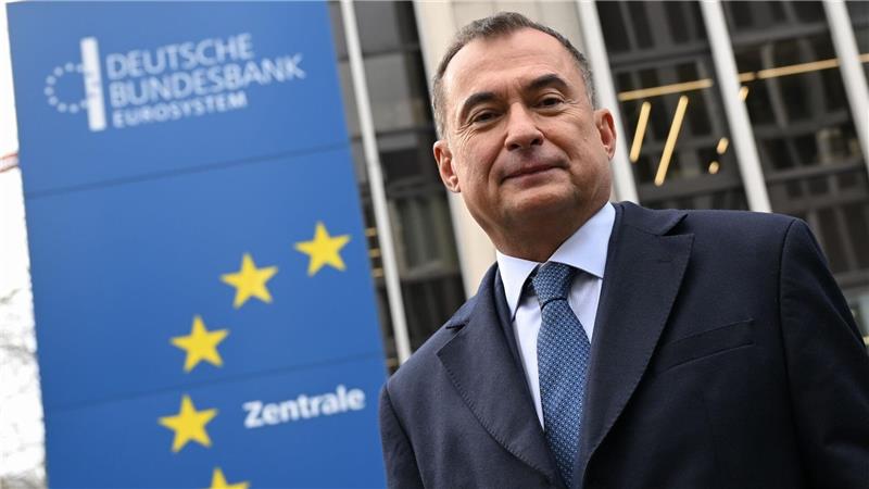 Mann im Anzug und Krawatte vor einem Gebäude mit einem Schild der Deutschen Bundesbank und gelben Sternen der Europaflagge