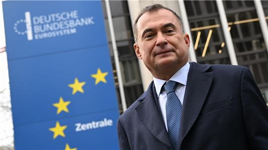 Mann im Anzug und Krawatte vor einem Gebäude mit einem Schild der Deutschen Bundesbank und gelben Sternen der Europaflagge