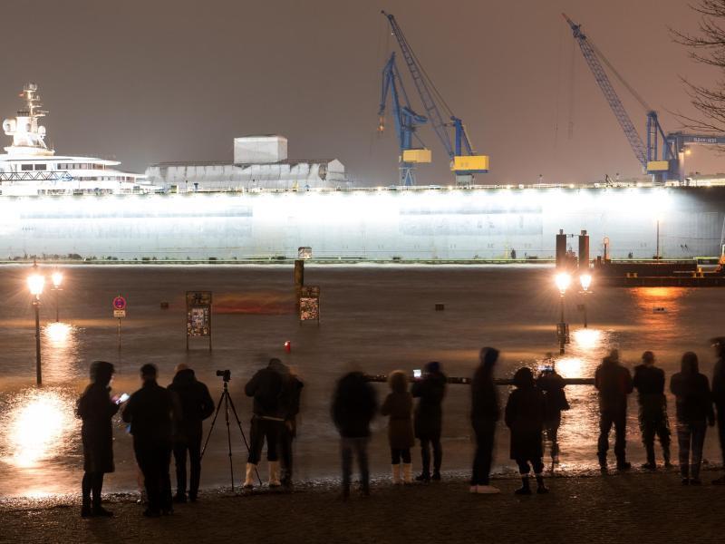 Passanten beobachten den während einer Sturmflut unter Wasser stehenden Fischmarkt an der Elbe. Foto: Daniel Bockwoldt/dpa