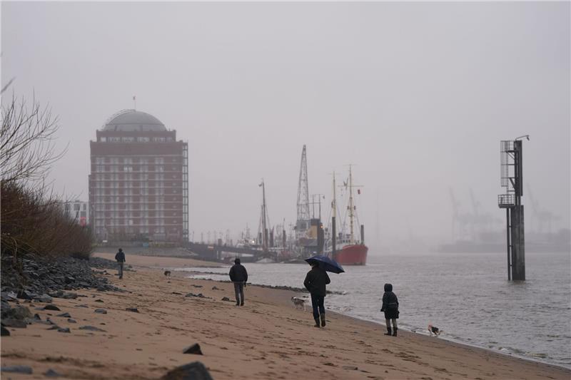Passanten gehen im strömenden Regen am Elbstrand in Ovelgönne spazieren.